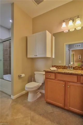 Full bathroom with tile patterned floors, toilet, vanity, and shower / bath combination with glass door