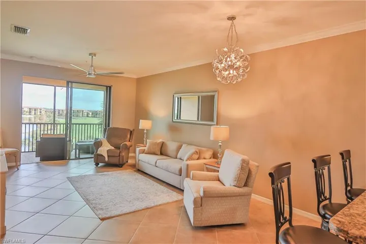 Living room with ornamental molding, light tile patterned flooring, and ceiling fan with notable chandelier