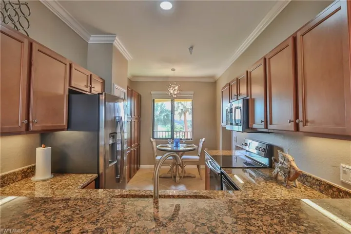 Kitchen with stainless steel appliances, a notable chandelier, sink, stone counters, and crown molding
