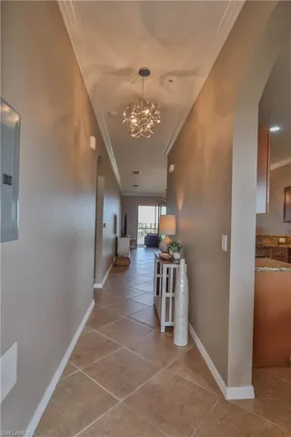 Hallway with ornamental molding, electric panel, an inviting chandelier, and light tile patterned floors