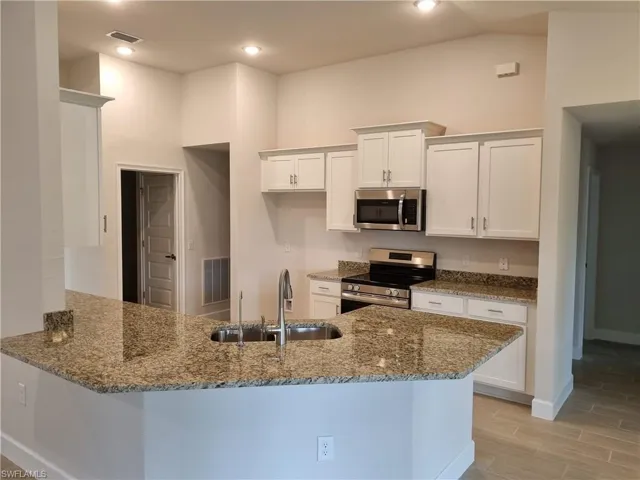 Kitchen featuring appliances with stainless steel finishes, sink, kitchen peninsula, dark stone countertops, and white cabinetry