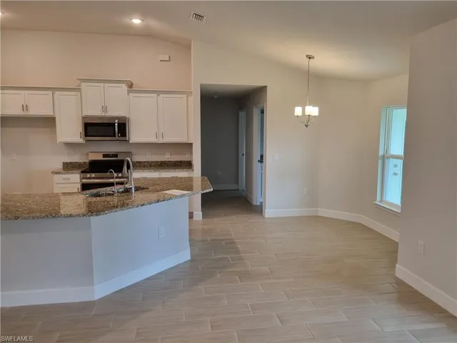 Kitchen featuring white cabinetry, dark stone counters, stainless steel appliances, pendant lighting, and vaulted ceiling