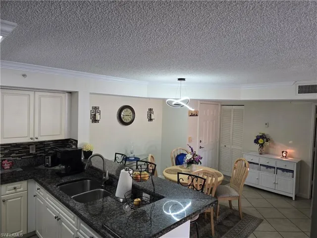 Kitchen featuring a textured ceiling, a sink, a peninsula, ornamental molding, and light tile patterned flooring