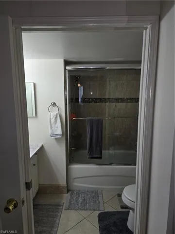 Full bath featuring tile patterned flooring, vanity, toilet, baseboards, and combined bath / shower with glass door