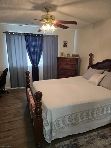 Bedroom with a textured ceiling, ceiling fan, dark wood finished floors, and a desk