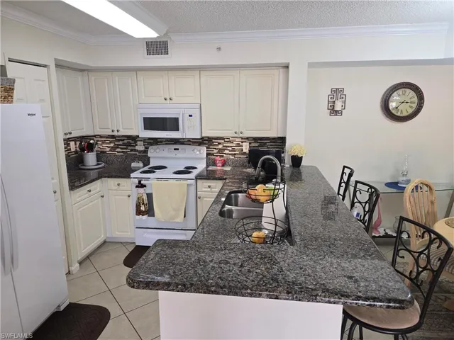 Kitchen with a sink, white appliances, a peninsula, tasteful backsplash, and visible vents