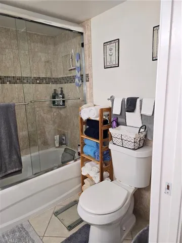 Bathroom featuring combined bath / shower with glass door, tile patterned floors, and toilet