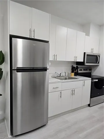 Kitchen featuring sink, range, stainless steel refrigerator, light hardwood / wood-style floors, and white cabinets