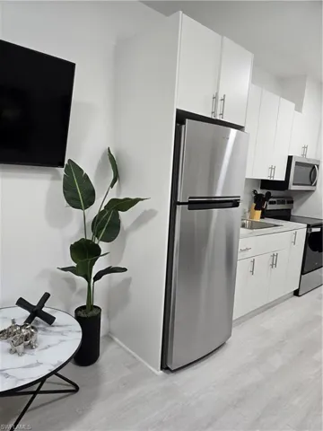 Kitchen featuring sink, stainless steel refrigerator, stove, white cabinets, and light wood-type flooring