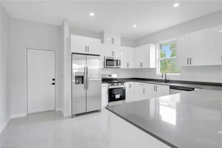 Kitchen featuring appliances with stainless steel finishes, white cabinets, light tile patterned flooring, recessed lighting, and dark stone counters