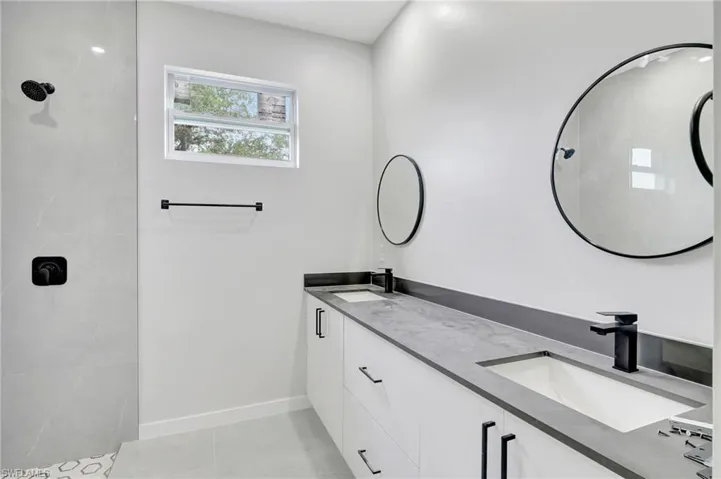 Bathroom with double vanity, tiled shower, and light tile patterned floors
