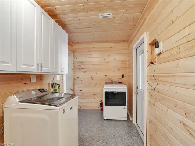 Laundry area with wood ceiling, washing machine and dryer, wooden walls, and cabinets