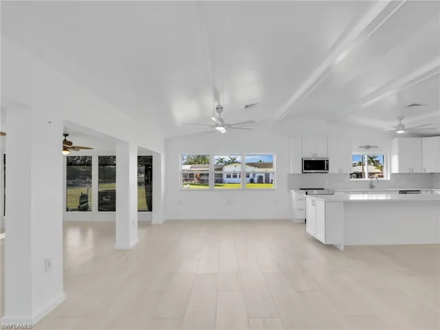 Kitchen featuring lofted ceiling with beams, a healthy amount of sunlight, white cabinetry, and light hardwood / wood-style flooring