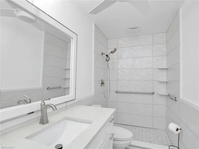 Bathroom featuring toilet, vanity, and tiled shower