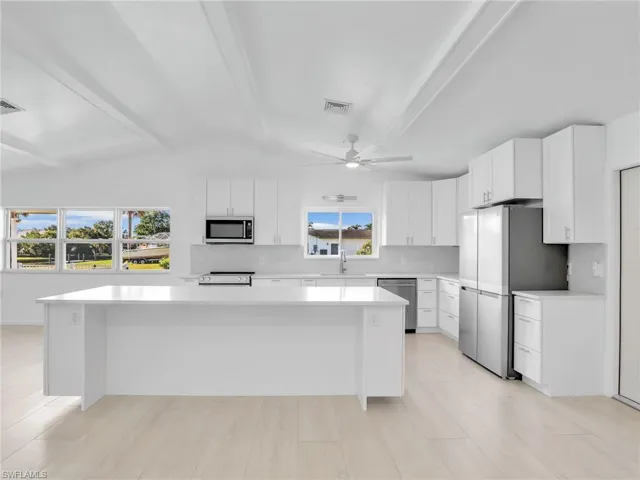 Kitchen featuring a center island, sink, lofted ceiling with beams, white cabinets, and appliances with stainless steel finishes