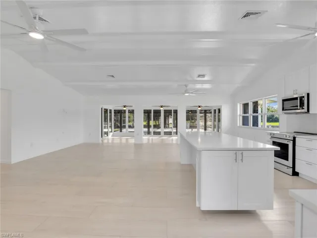 Kitchen featuring lofted ceiling with beams, light wood-type flooring, a kitchen island, white cabinetry, and stainless steel appliances