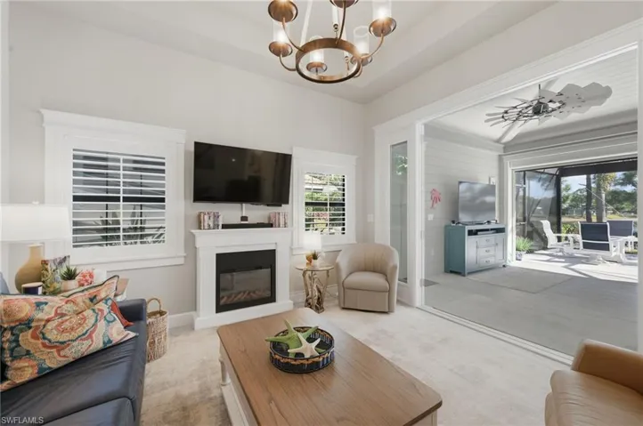 Living room featuring a chandelier, carpet, a ceiling fan, and a glass covered fireplace