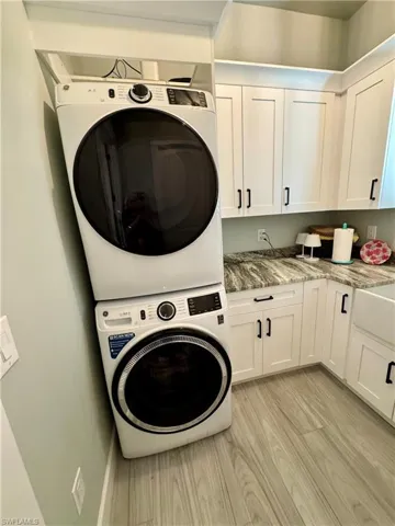 Kitchen featuring stainless steel appliances, light stone counters, decorative light fixtures, white cabinets, and a sunroom