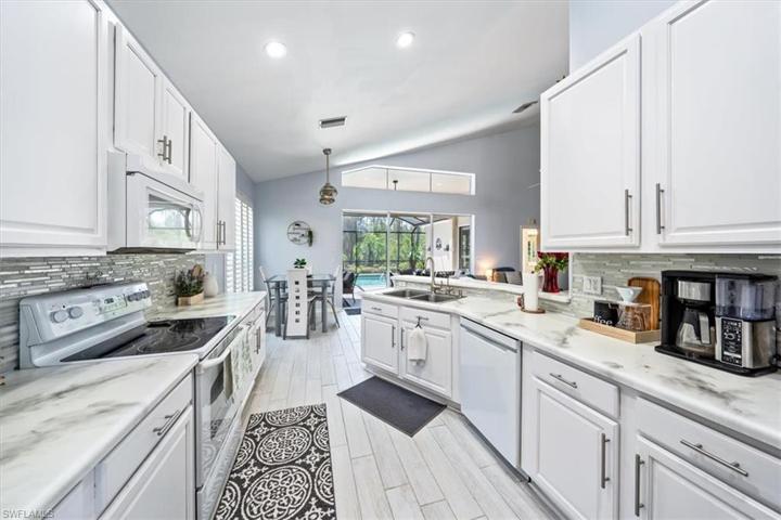 Wood look plank tile flooring continues through to the kitchen, which features white cabinetry, glass backsplash, and ample countertop space.