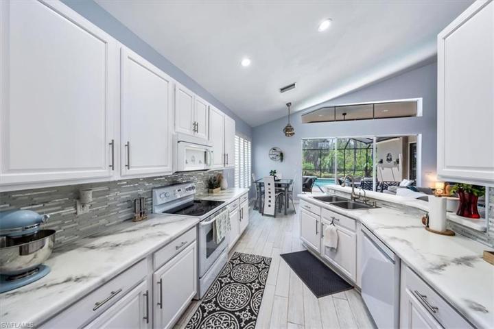Wood look plank tile flooring continues through to the kitchen, which features white cabinetry, glass backsplash, and ample countertop space.