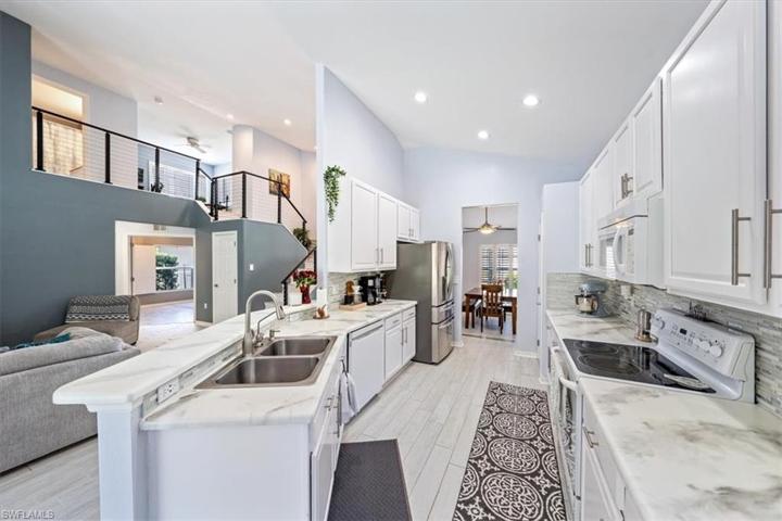 Wood look plank tile flooring continues through to the kitchen, which features white cabinetry, glass backsplash, and ample countertop space.
