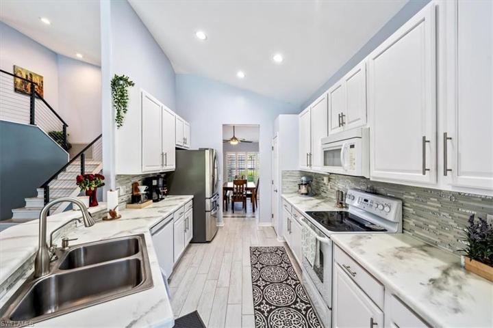 Wood look plank tile flooring continues through to the kitchen, which features white cabinetry, glass backsplash, and ample countertop space.
