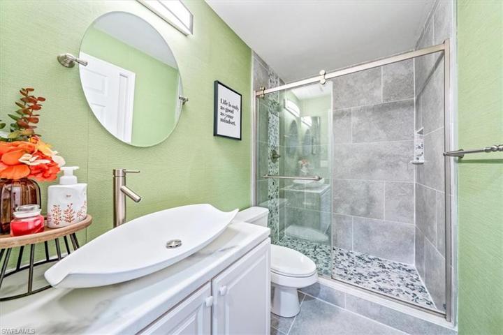The updated downstairs guest bath features a vessel sink, shower tile with flat river rock mosaic floor and listello, and barn door style shower glass.