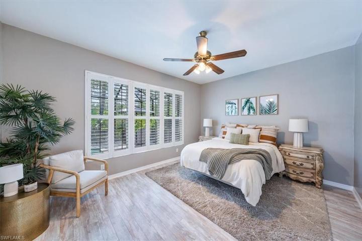 The primary bedroom features wood look plank tile flooring, a seating area, large windows overlooking the pool and sliders leading out to the covered living area.