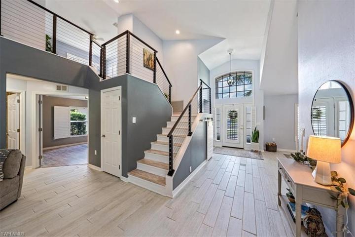 The light and bright two-story foyer and great room feature wood look plank tile, a cable stair railing with catwalk, ample natural light, and storage space under the stairs with decorative barn door entry.
