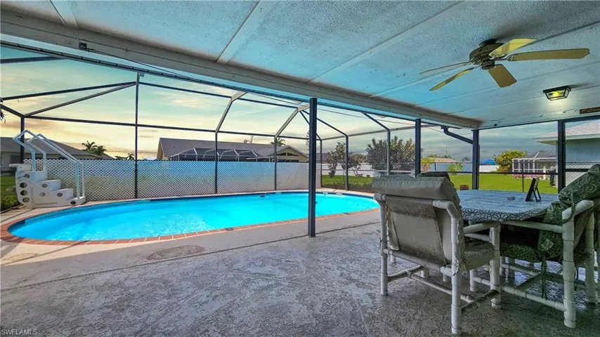 Pool at dusk featuring glass enclosure, ceiling fan, and a patio area