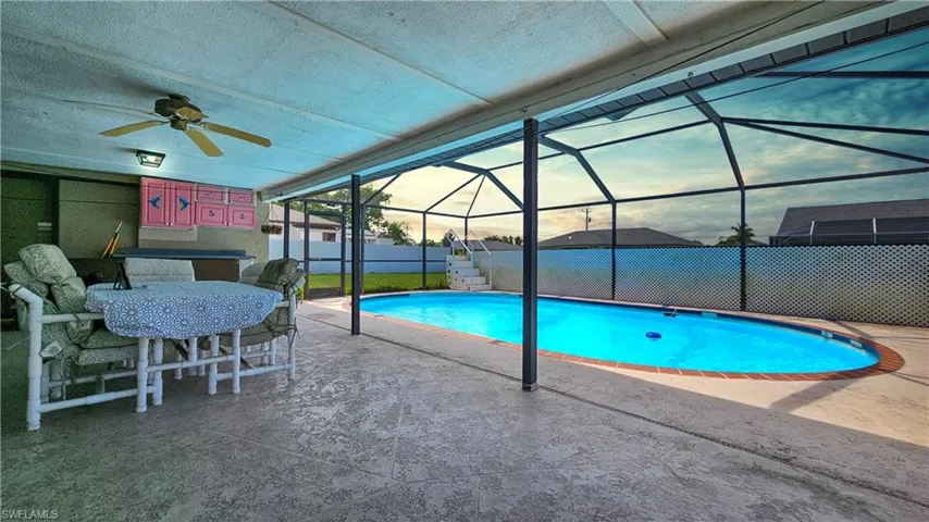 Pool at dusk with a patio, glass enclosure, and ceiling fan