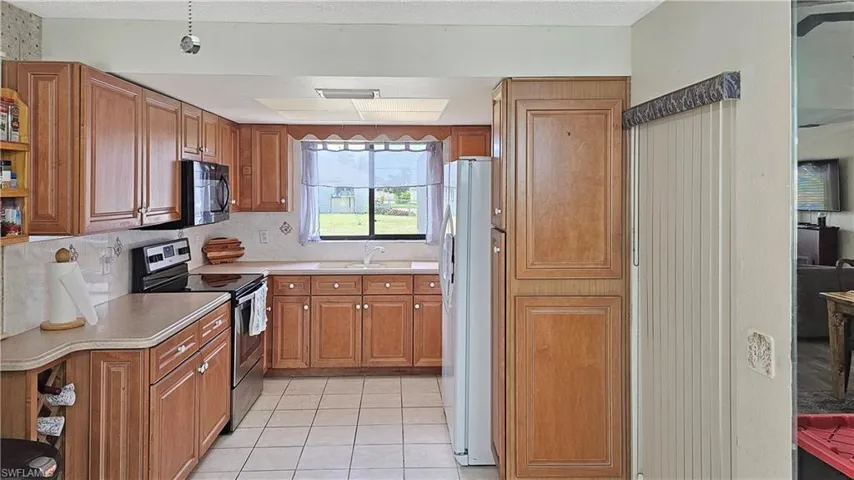 Kitchen with decorative backsplash, stainless steel range with electric stovetop, sink, white refrigerator, and light tile patterned flooring