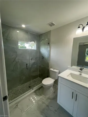 Bathroom featuring vanity, a stall shower, marble finish flooring, healthy amount of natural light, and recessed lighting