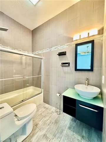 Bathroom with tile walls, shower / bath combination with glass door, vanity, and a textured ceiling