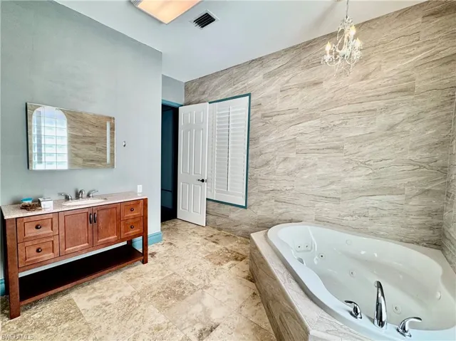 Bathroom with vanity, a tub with jets, and a chandelier