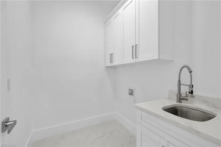 Laundry area featuring sink, washer hookup, light tile patterned floors, and cabinets