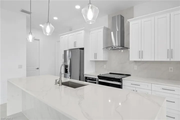Kitchen with decorative light fixtures, wall chimney exhaust hood, light stone countertops, stainless steel appliances, and a large island