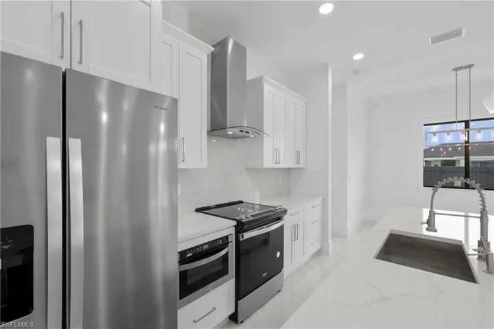 Kitchen featuring sink, decorative backsplash, light stone counters, stainless steel appliances, and wall chimney range hood