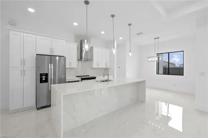 Kitchen with wall chimney range hood, pendant lighting, light tile patterned floors, sink, and stainless steel fridge with ice dispenser