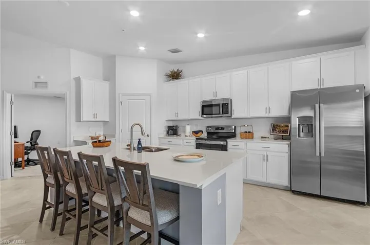 Kitchen featuring a breakfast bar area, an island with sink, sink, white cabinetry, and appliances with stainless steel finishes
