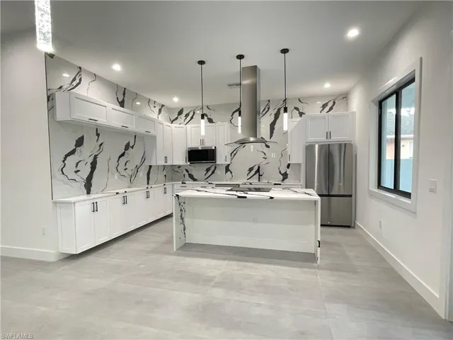 Kitchen featuring backsplash, stainless steel appliances, a center island, hanging light fixtures, and white cabinets
