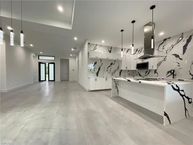 Kitchen with island range hood, decorative light fixtures, white cabinets, and tasteful backsplash