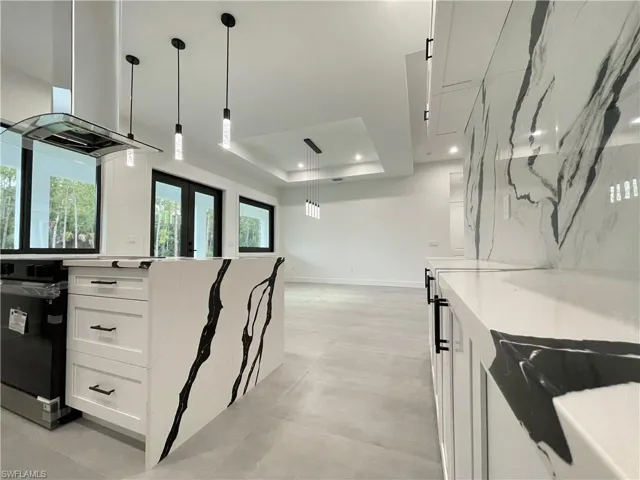 Kitchen featuring oven, light stone countertops, white cabinetry, a raised ceiling, and pendant lighting