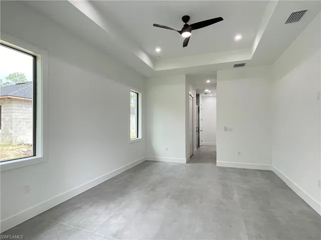 Unfurnished room featuring a tray ceiling, a healthy amount of sunlight, concrete flooring, and ceiling fan