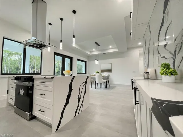 Kitchen featuring pendant lighting, island exhaust hood, white cabinetry, a tray ceiling, and light stone countertops