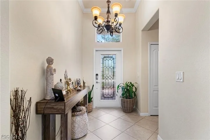 Foyer featuring a chandelier, crown molding, a textured wall, a high ceiling, and light tile patterned floors