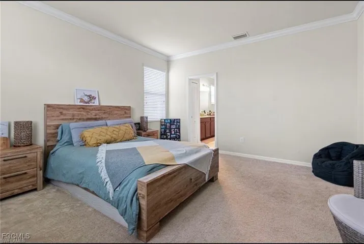 Bedroom with light colored carpet, ornamental molding, and ensuite bath