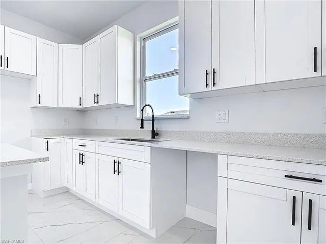 Kitchen featuring white cabinetry, light stone counters, and light marble finish flooring