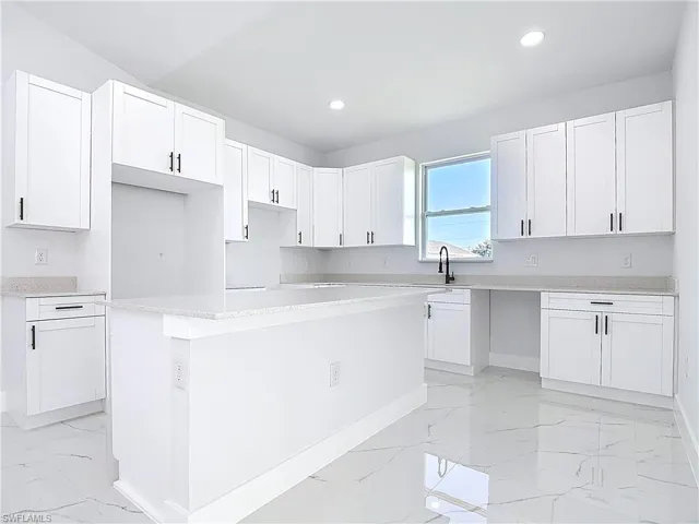 Kitchen with light marble finish floors, white cabinetry, a kitchen island, light stone counters, and recessed lighting
