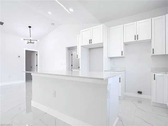 Kitchen with light marble finish flooring, white cabinets, light stone counters, a chandelier, and high vaulted ceiling